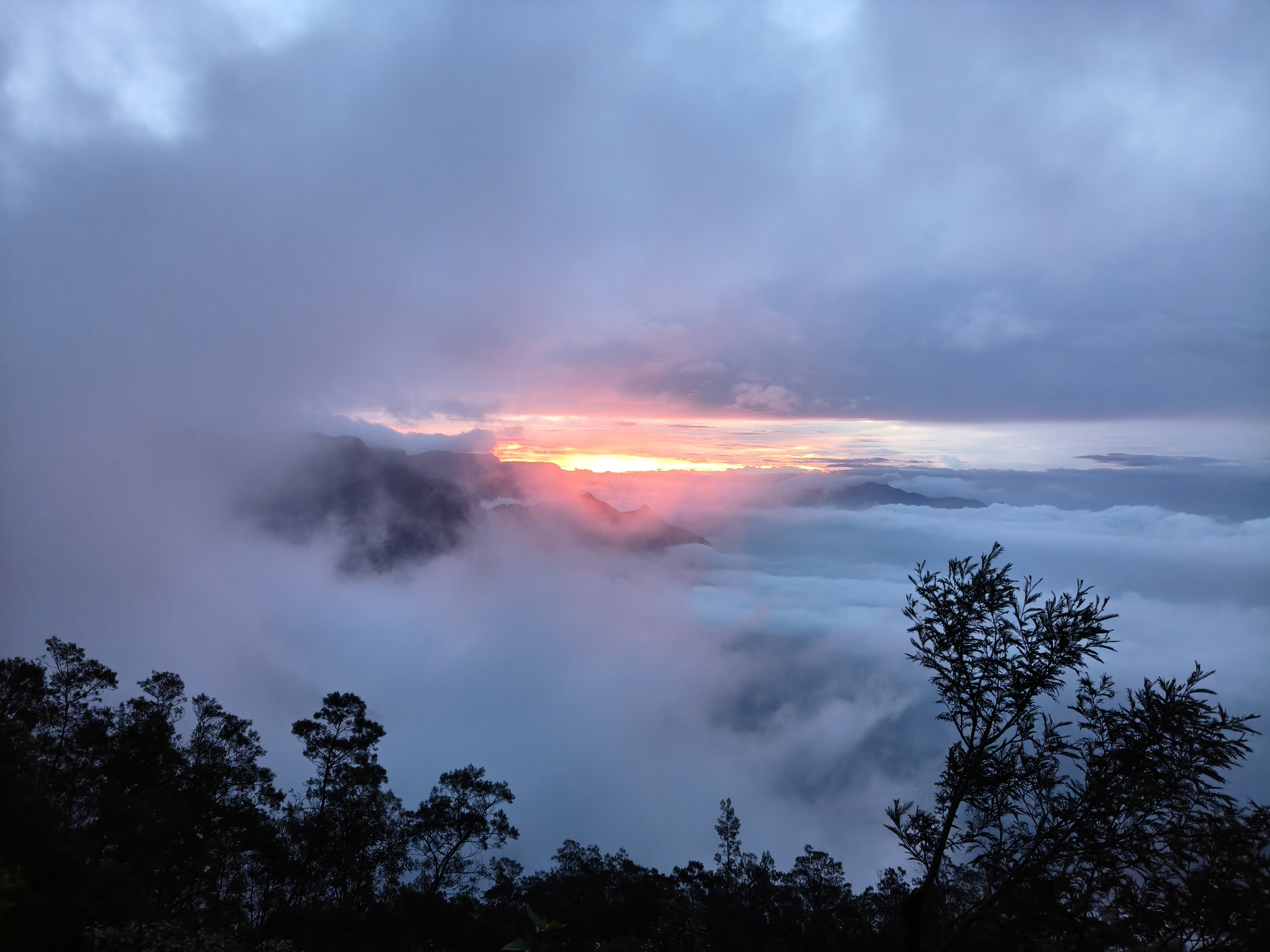 Kolukkumalai sunrise through thick mist clouds over mountain peaks